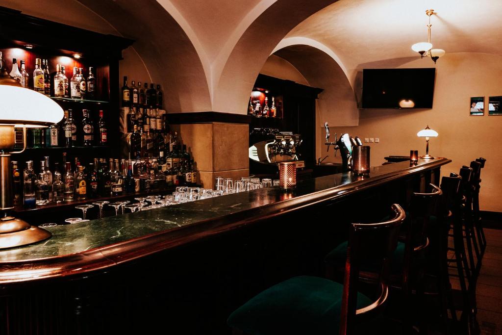 dimly lit hotel bar with marble countertop, rows of bottles, wooden bar stools, arched ceiling