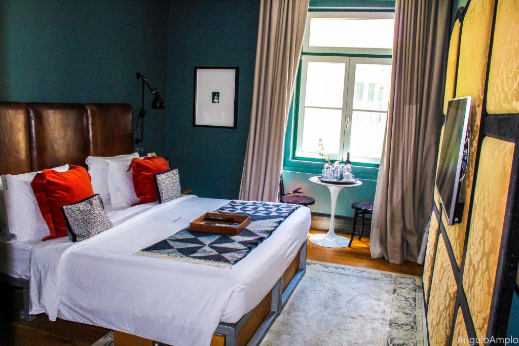 A dark-accented bedroom with red cushions, a large window and a small refreshment table.
