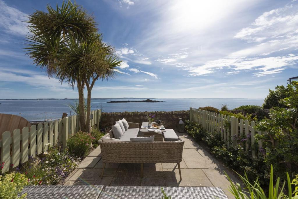 a patio with a couch and a palm tree and the ocean at Mariners Cottage in Mousehole
