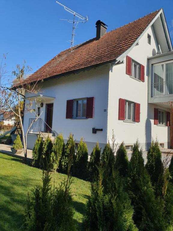 een wit huis met rode luiken en een tuin bij Ferienwohnung Suppan in Hörbranz