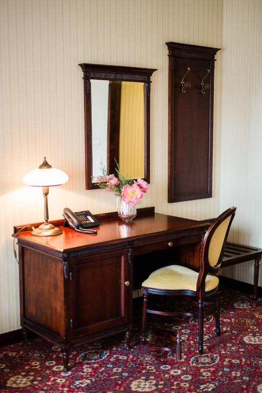 Classic wooden desk and upholstered chair with lamp, mirror, and fresh flowers, cozy workspace