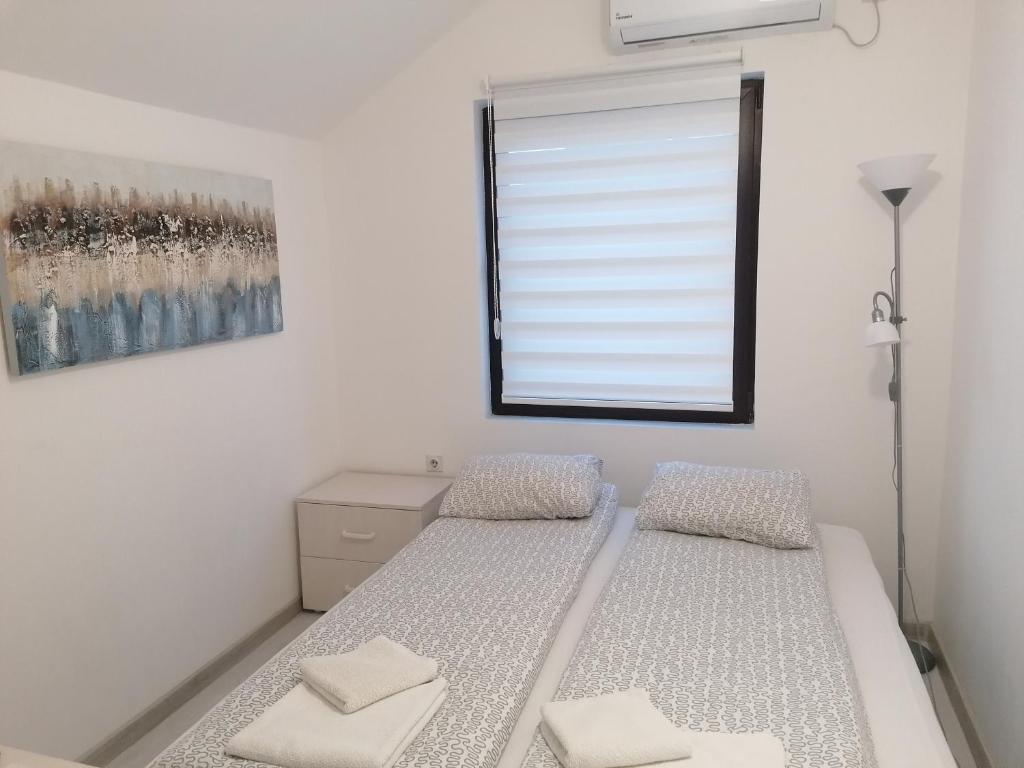 a white bedroom with two beds and a window at Apartman Andrijana 1 in Soko Banja