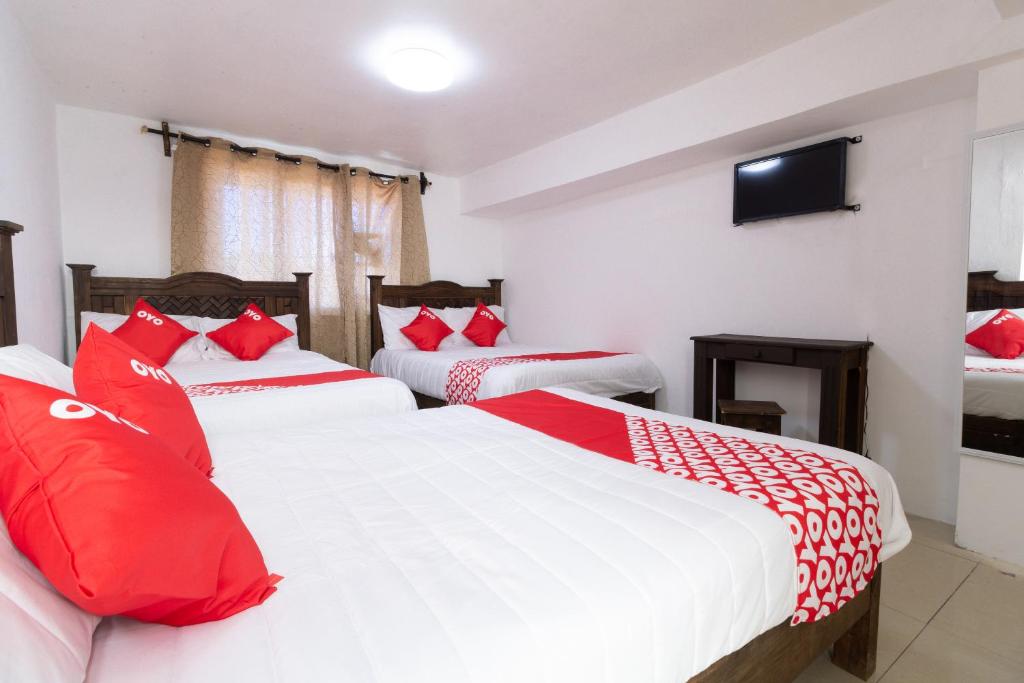 a bedroom with two beds with red pillows and a tv at OYO Hotel Punta Guadalupe, San Cristóbal de las Casas in San Cristóbal de Las Casas