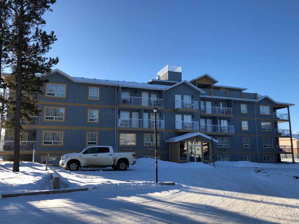 un gran edificio de apartamentos con un camión estacionado en la nieve en Misty Mountain Inn & Suites, en Grande Cache