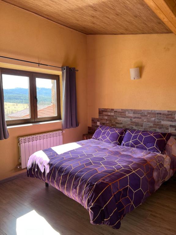 ein Schlafzimmer mit einem Bett mit lila Daunendecke und einem Fenster in der Unterkunft Casa Rural La Colmena in Condemios de Abajo