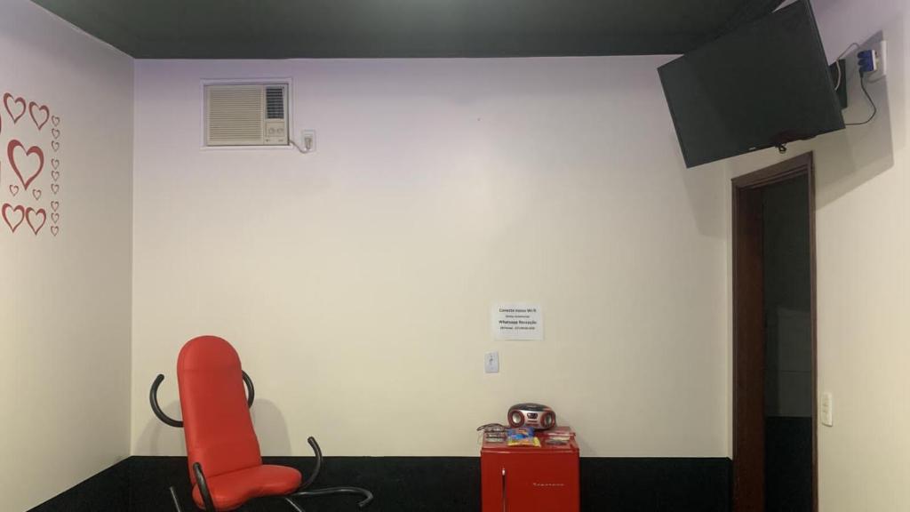 a room with a red chair and a white wall at Versat Motel in Barretos