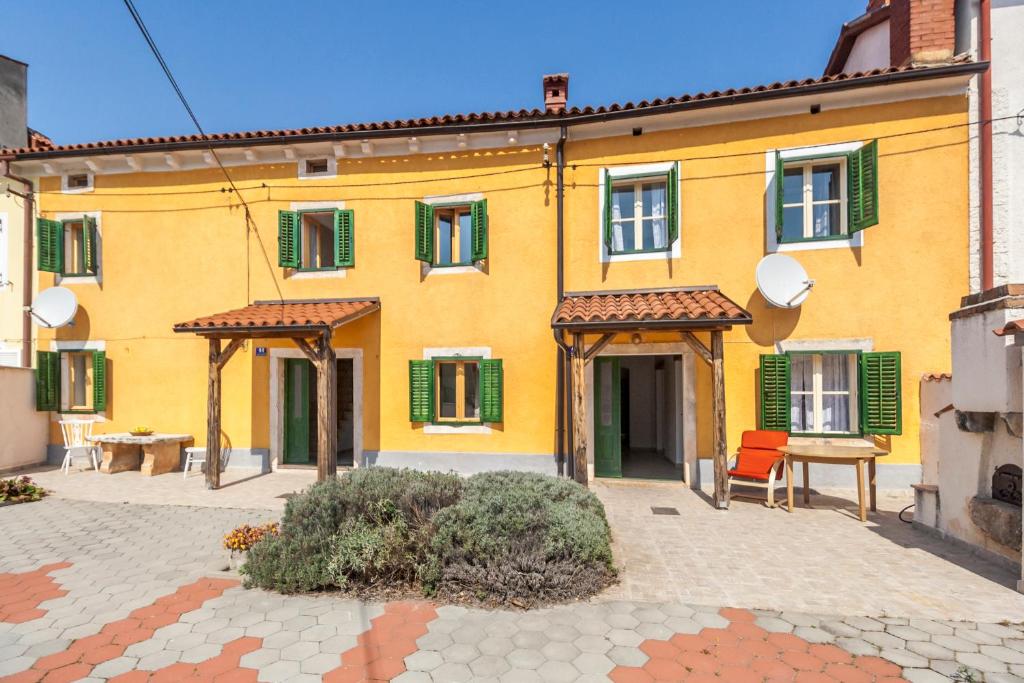 una casa gialla con finestre con persiane verdi e una sedia di House Krizanic in Marčana, Istria, with 2 apartments, total 9 guests a Marčana