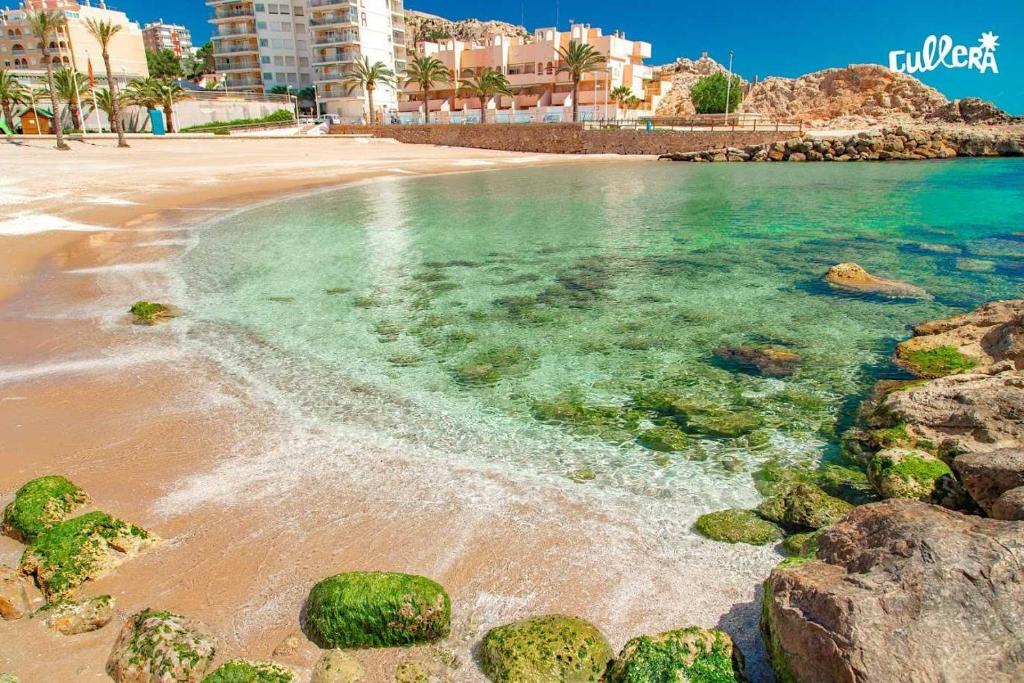 een strand met rotsen in het water en gebouwen bij Fantastico apartamento Faro de cullera a primera linea mar abierto playa de los olivos in Faro de Cullera