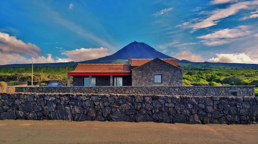 a house behind a stone wall with a mountain in the background at Yes Pico - By the Sea "Casa 3 Vistas" in Santa Luzia
