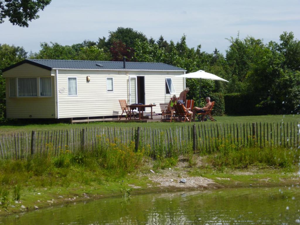 une caravane blanche avec une table, des chaises et un parasol dans l'établissement Chalet, à Wilbertoord