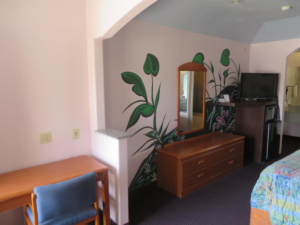 a hotel room with a bed and a dresser and a mirror at Travelers Inn and Suites Liberty in Liberty