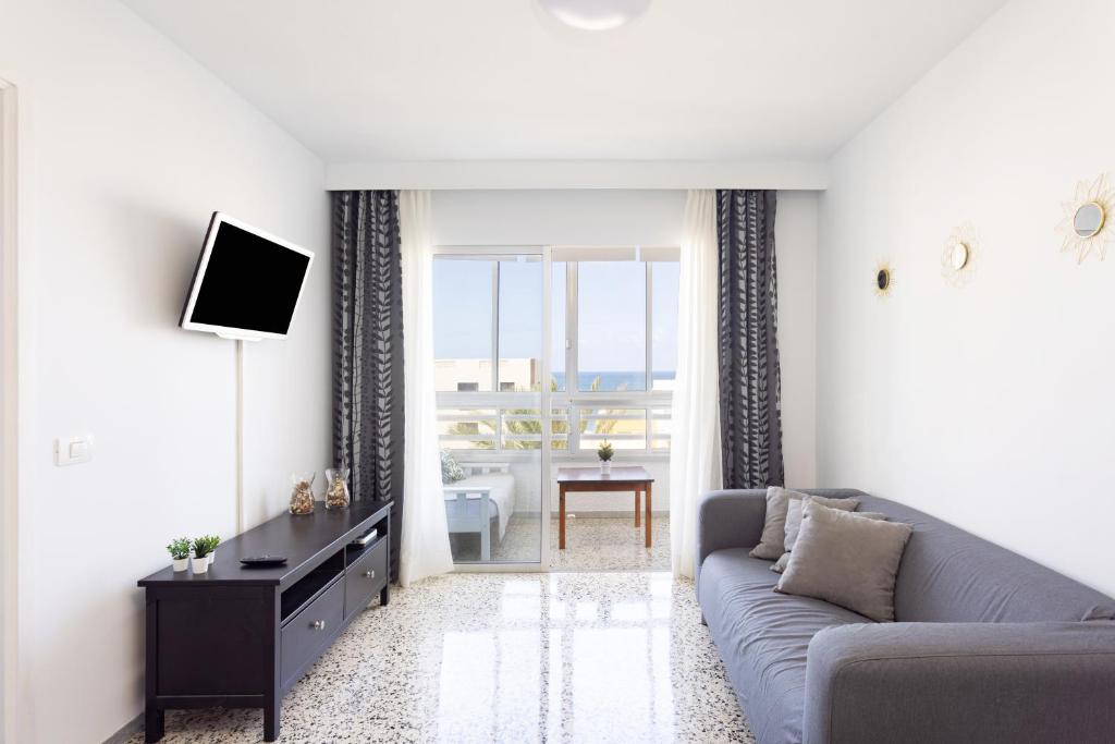 ein Wohnzimmer mit einem grauen Sofa und einem TV in der Unterkunft Home2Book Apartamento Vista al Mar in Bajamar