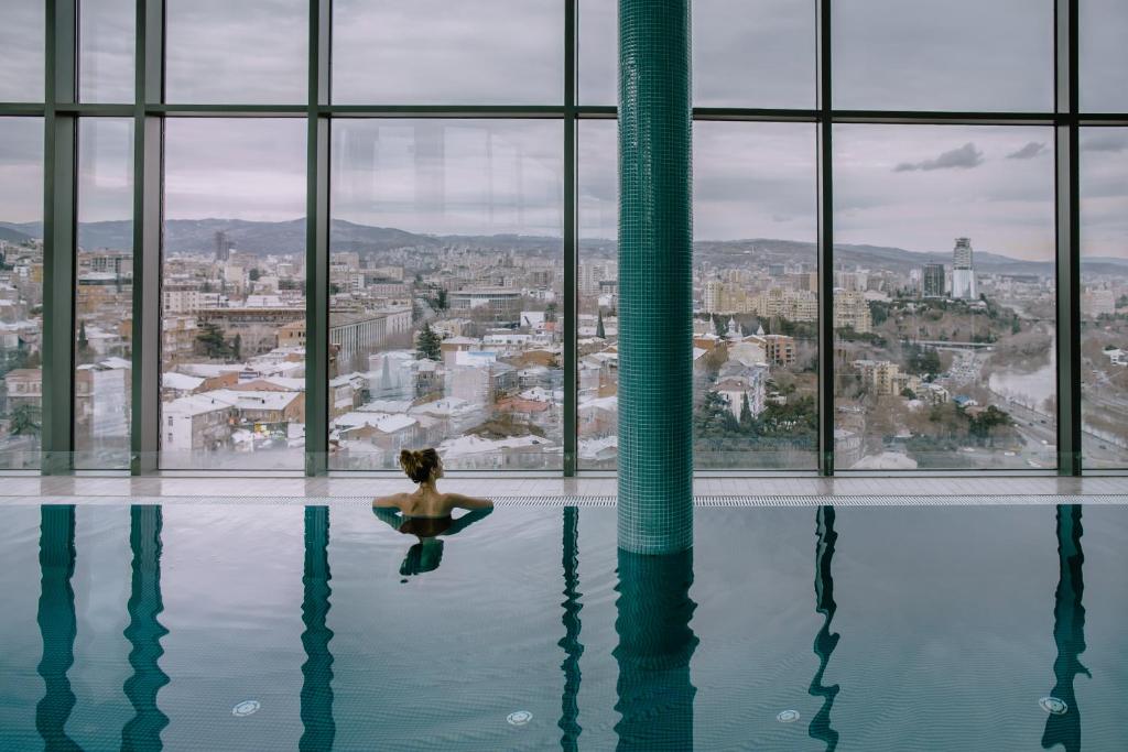 una donna in piscina con vista sulla città di Radisson Blu Iveria Hotel a Tbilisi City