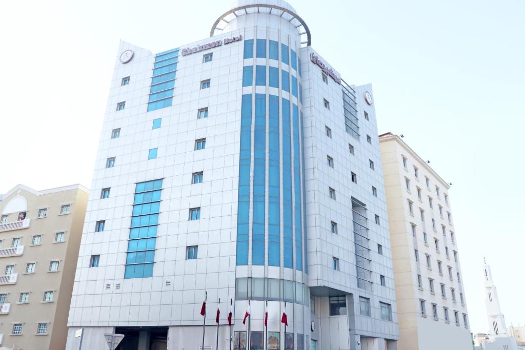 Um edifício alto e branco com bandeiras vermelhas à frente. em Chairmen Hotel em Doha