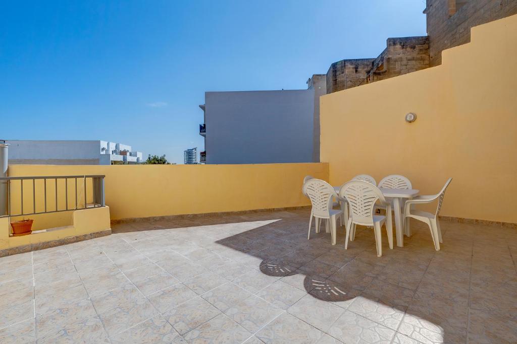 eine Terrasse mit weißen Stühlen und einem Tisch an einer gelben Wand in der Unterkunft Modern 2 Bedroom Maisonette in Central Sliema in Sliema