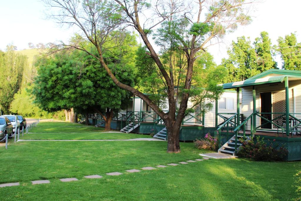 a green and white house with trees and lawn chairs at Gundagai Cabins & Tourist Park in Gundagai