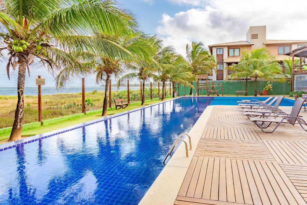 uma piscina com cadeiras e palmeiras junto ao oceano em IT12 Lindo Bangalô Duplex 2 Suítes Pé na Areia, Itacimirim em Itacimirim