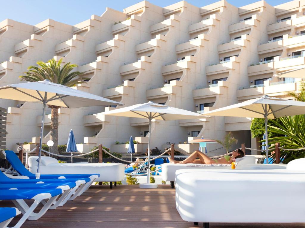 a hotel with lounge chairs and umbrellas in front of it at Alexandre Grand Teguise Playa in Costa Teguise