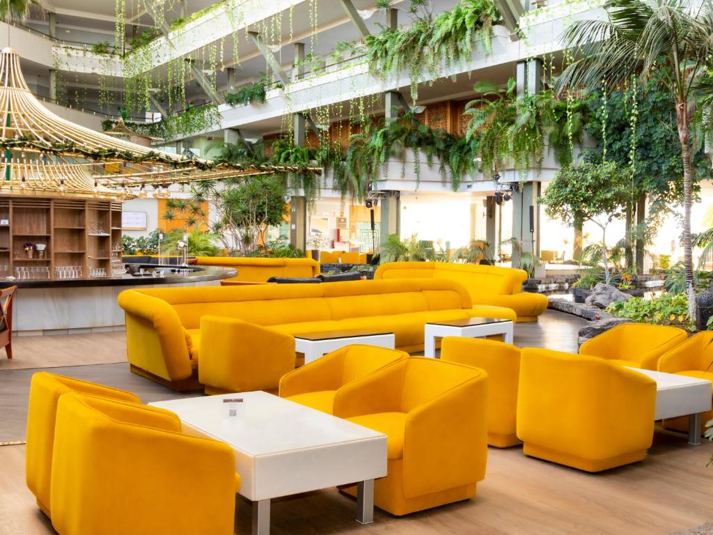 a lobby with yellow couches and tables and plants at Alexandre Grand Teguise Playa in Costa Teguise