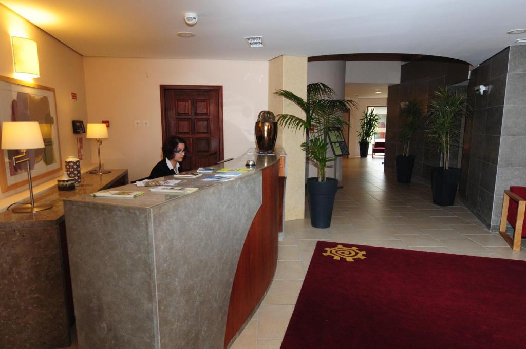 uma mulher sentada num balco no trio de um hotel em INATEL Linhares da Beira Hotel Rural em Linhares