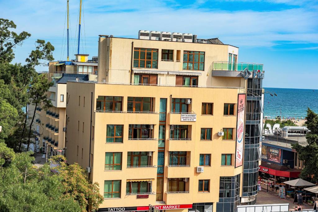 a yellow building with the ocean in the background at Menada Midia Apartments in Sunny Beach