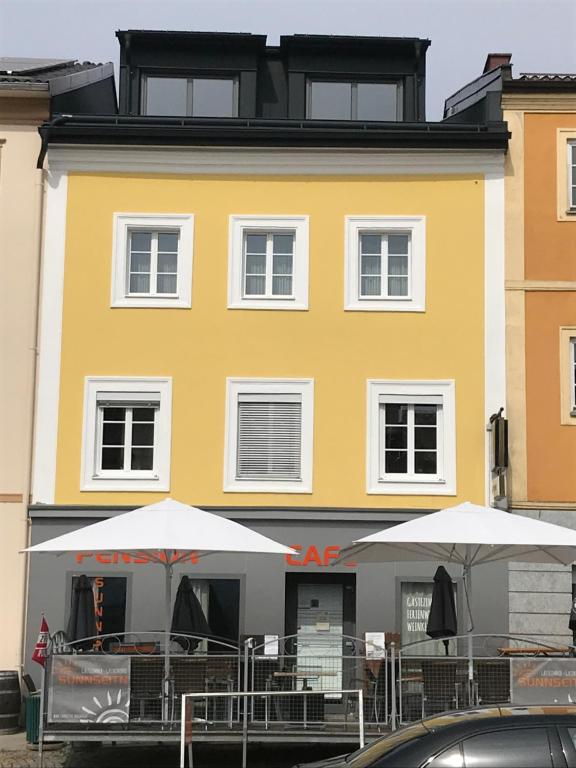 een geel gebouw met tafels en parasols ervoor bij Pension Sunnseitn - Gasthof - Café - Weinkeller in Haslach an der Mühl