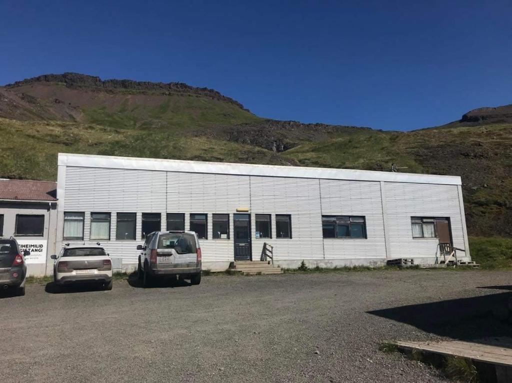 ein weißes Gebäude mit Autos auf einem Parkplatz in der Unterkunft Gistiheimilið Bergistangi 2 in Norðurfjörður