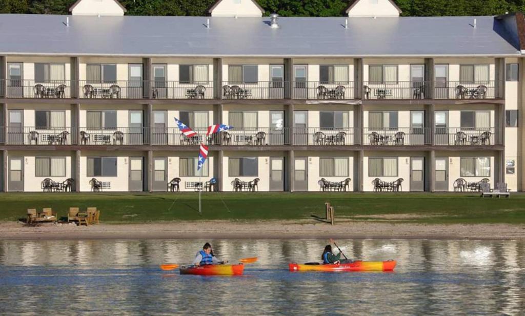 dos personas en kayaks en el agua frente a un edificio en Bavarian Haus Lakefront Inn, en Saint Ignace