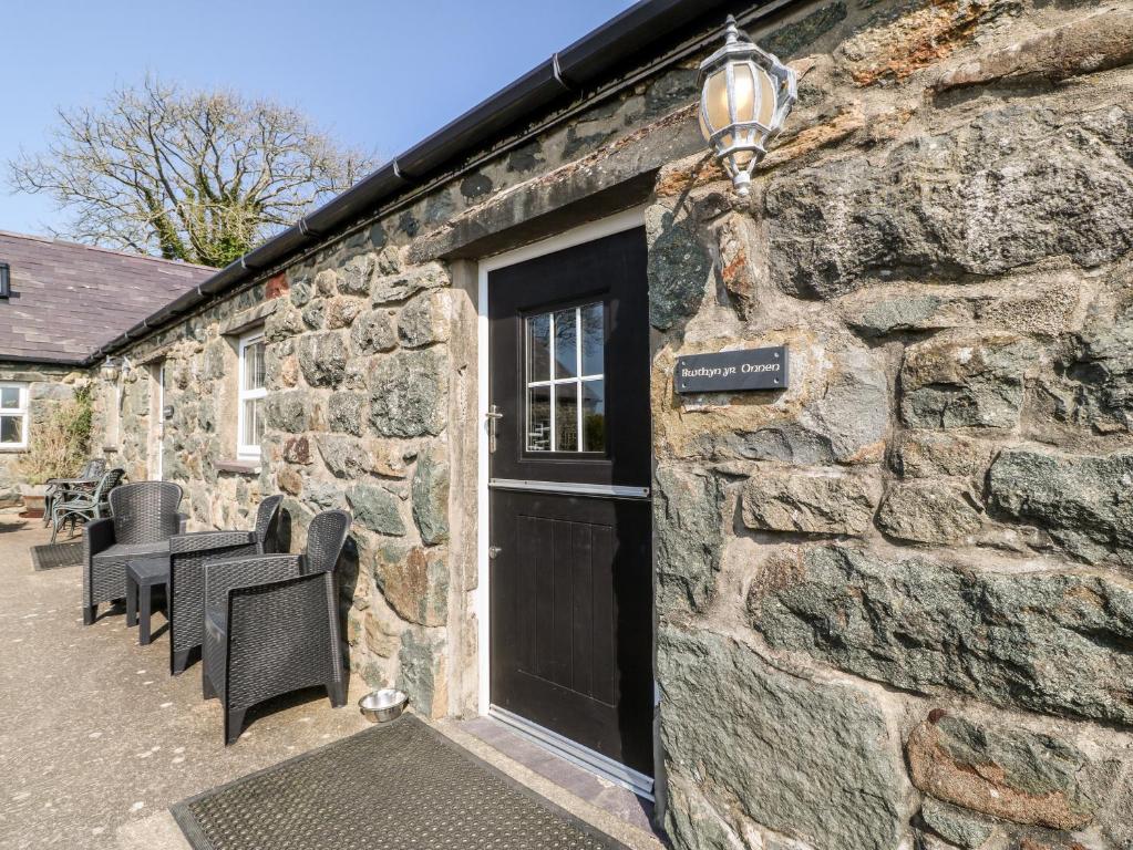 a stone building with a black door and chairs at Bwthyn yr Onnen Ash Cottage in Llannor