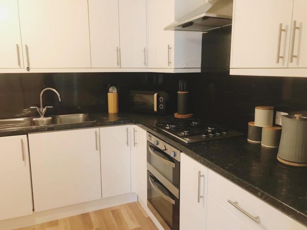a kitchen with white cabinets and a black counter top at JB Stays Family & contractor stays, Free parking in London