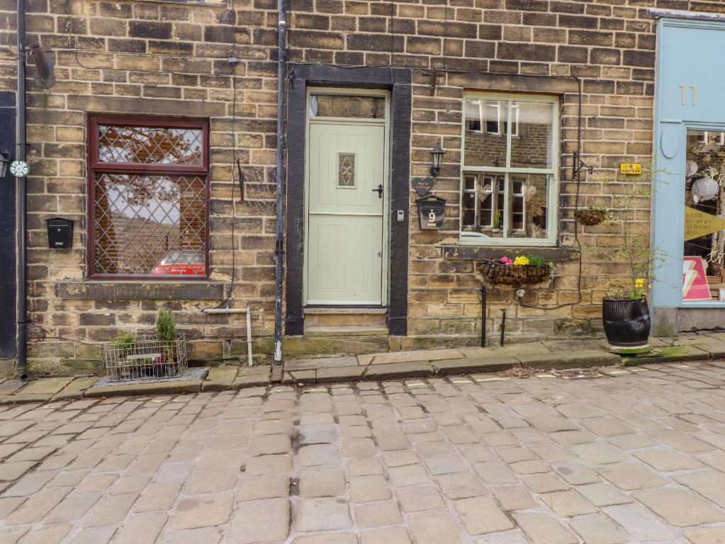 ein Backsteinhaus mit einer weißen Tür und Fenstern in der Unterkunft Maria Cottage in Haworth