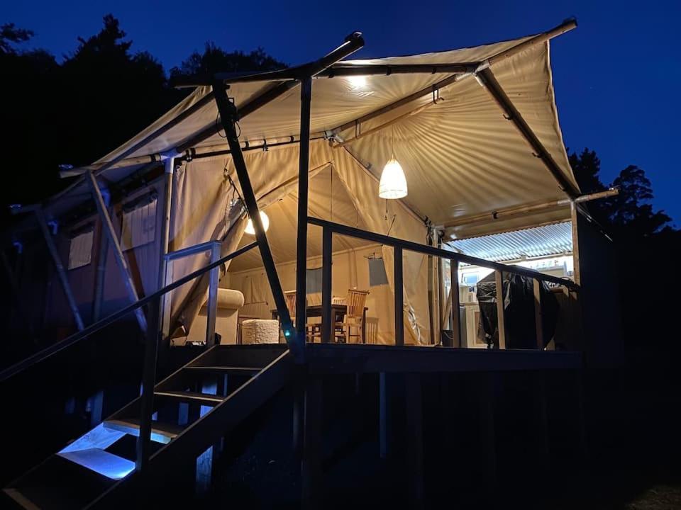 a tent with a table and chairs in it at night at Lynx Lodge in Waipapa