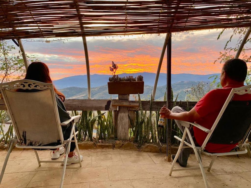 un hombre y una mujer sentados en sillas mirando la puesta de sol en Hotel SPA Campestre Los Adobes en Taxco de Alarcón