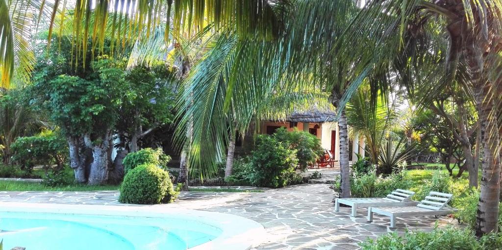 a swimming pool with two benches and a house at Watamu Villa With Service Personnel in Watamu