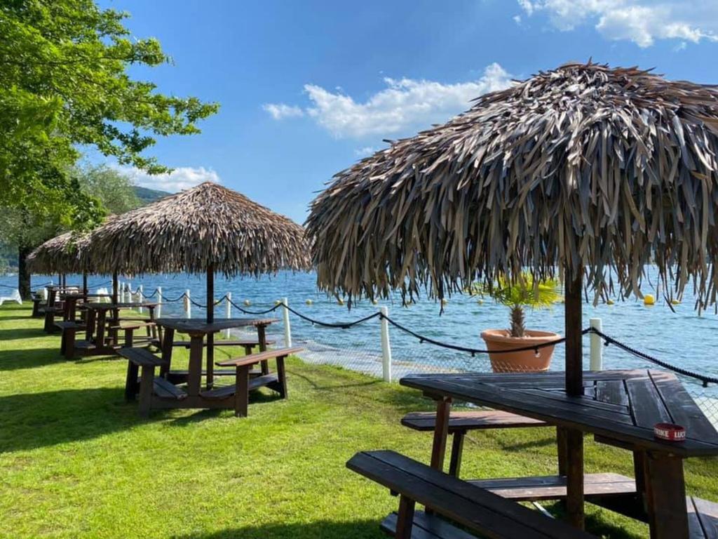 a row of picnic tables with straw umbrellas next to the water at Brand New Apartmentcecilia Residence Apt N5 in Agno