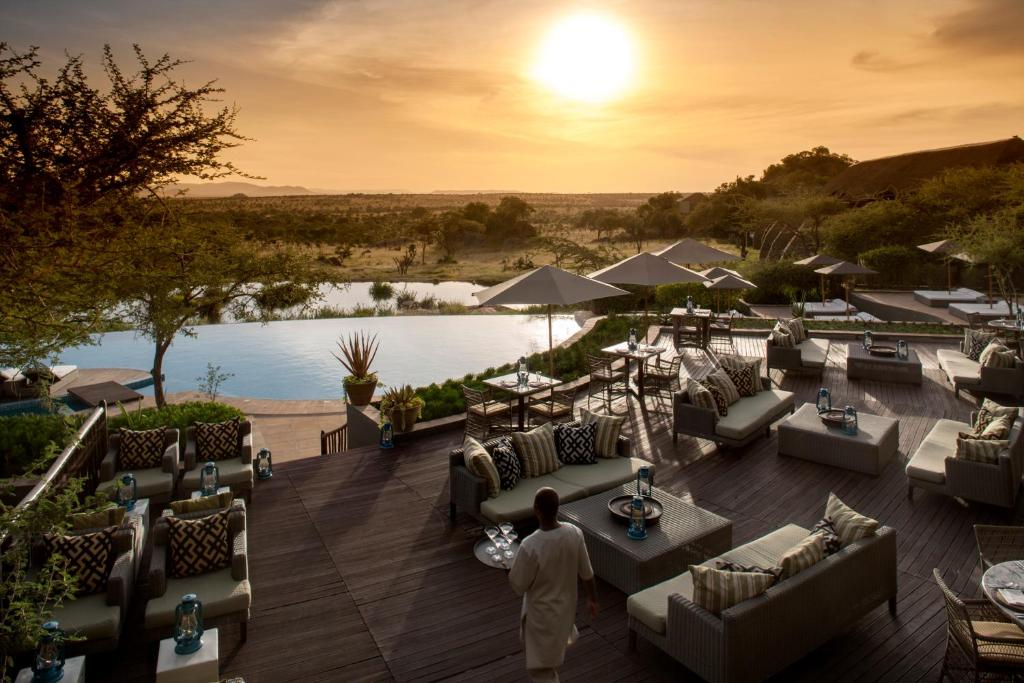 een man staat op een dek met banken en tafels bij Four Seasons Safari Lodge Serengeti in Banagi