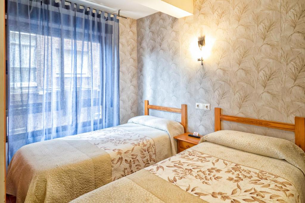 two beds in a room with a window at Pension La Playa in Talavera de la Reina