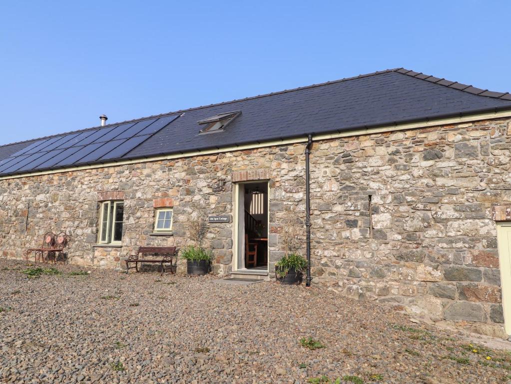 a stone house with a black roof and a patio at Old Spot Cottage in Goodwick