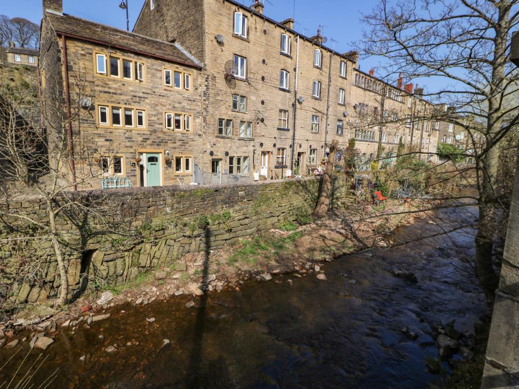 ein großes Backsteingebäude neben einem Fluss in der Unterkunft Kingfisher Cottage in Holmfirth