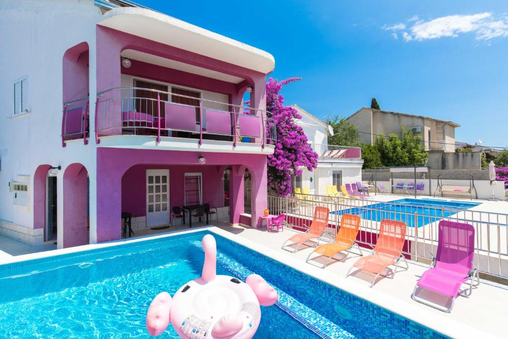 a pink house with a swimming pool and chairs at Beachfront villas Pinky-Superior heated pools and jacuzzi just 25 m from see in Seget Vranjica