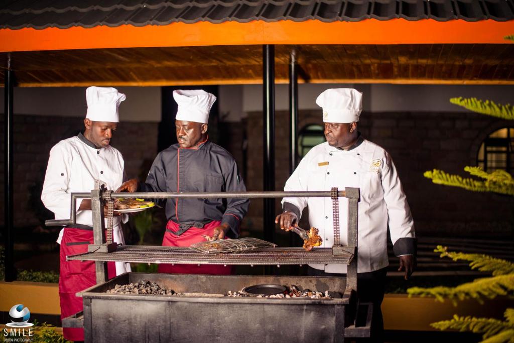 three chefs standing in a kitchen preparing food on a grill at TURACO INTERCOUNTY RESORT in Maragoli