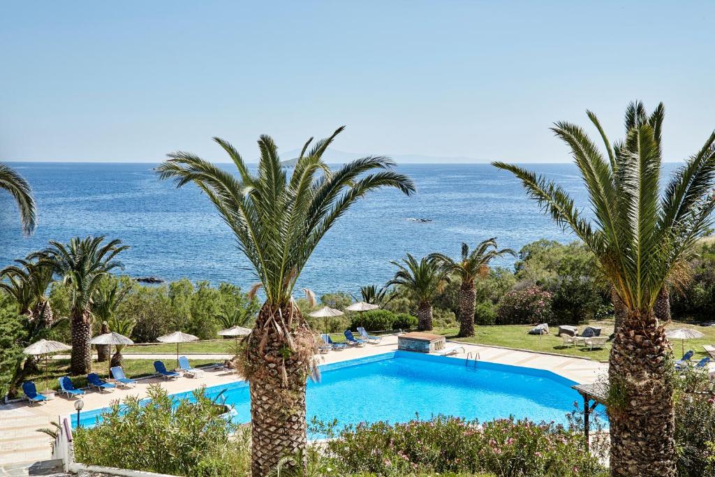 einen Pool mit Palmen und dem Meer im Hintergrund in der Unterkunft Andros Holiday Hotel in Gavrio