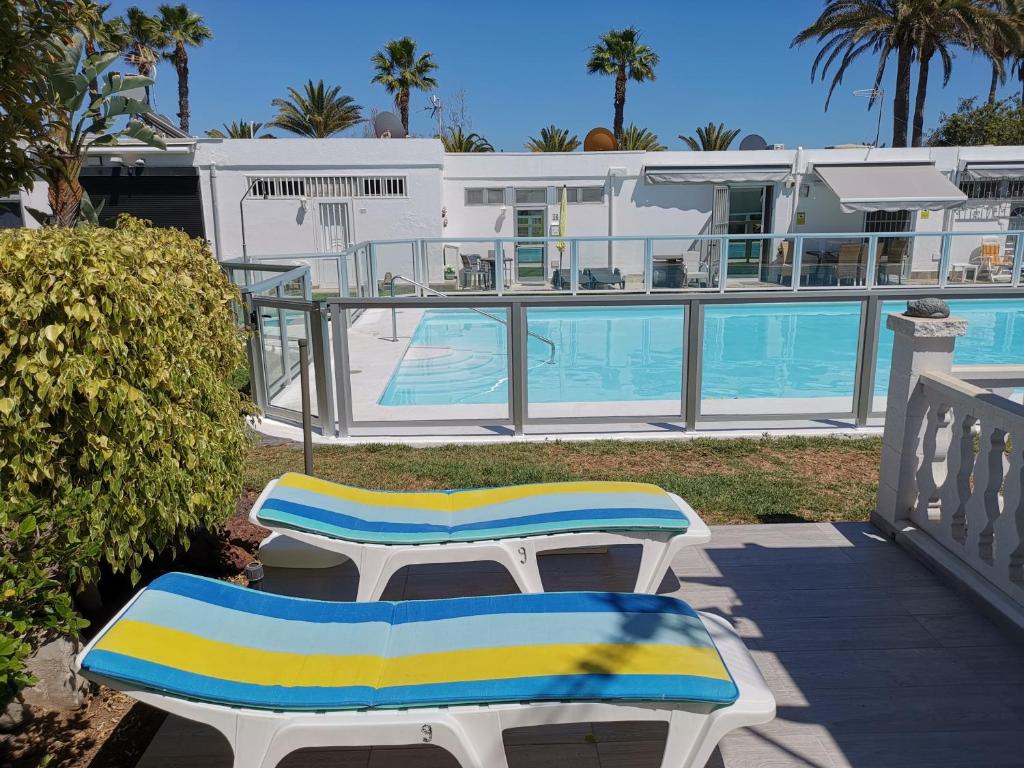 two lounge chairs sitting on a porch next to a swimming pool at Seaside bungalow in Maspalomas