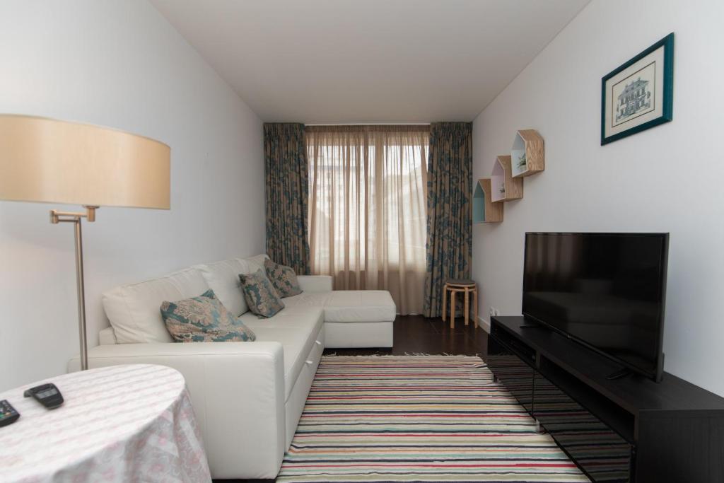 sala de estar con sofá blanco y TV de pantalla plana en Apartamento Luz T1 Sesimbra en Sesimbra