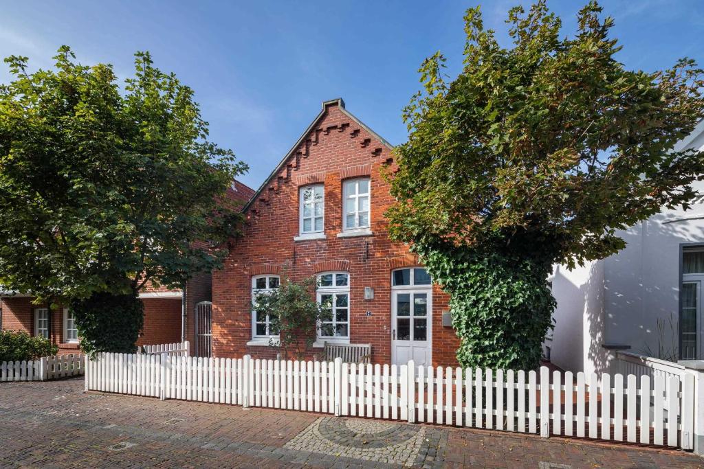 ein rotes Backsteinhaus mit einem weißen Zaun in der Unterkunft Rothen Huus in Norderney