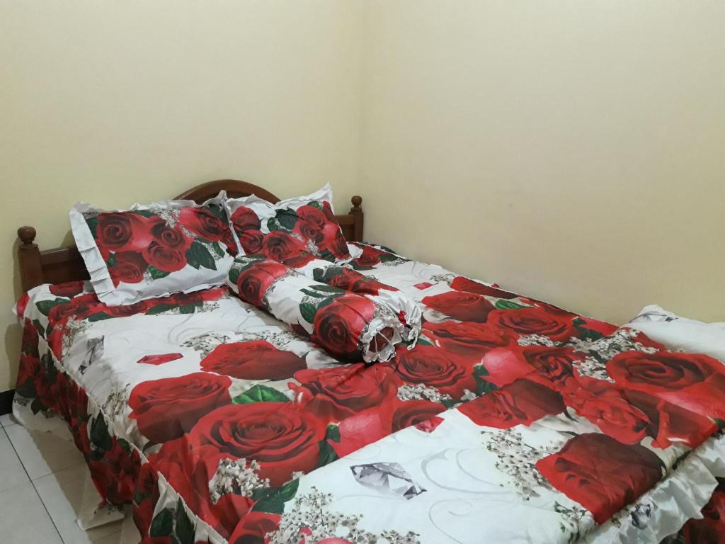 uma cama com uma colcha vermelha e branca com rosas vermelhas em OYO Homes 91083 Desa Wisata Plosokuning Syariah em Soprayan