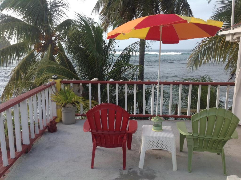 two chairs and an umbrella on a balcony with the ocean at Rainbow Beach Apartments & Rooms in Calibishie