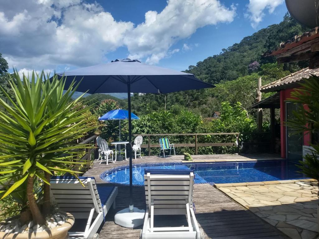 una piscina con 2 sillas y una sombrilla azul en Chalé Vale da Mata, en Visconde De Maua