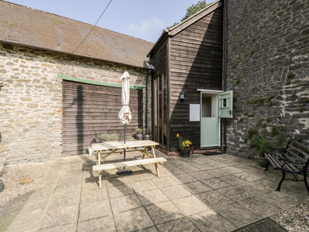 a patio with a wooden table and an umbrella at The Old School Room in Chelborough