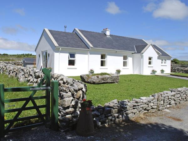 a white house with a stone wall and a fence at Dolmen Cottage in Kilfenora